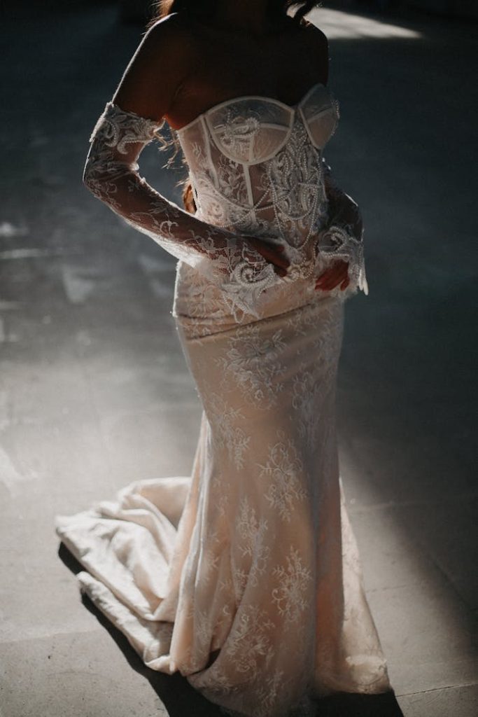 A beautifully detailed lace wedding dress worn by an adult female in soft, dramatic lighting.
