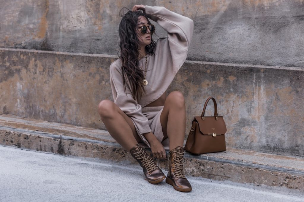Please help support by following @dayinmydreams on Instagram xoxo Girl with long hair sits on a cement street curb wearing a sweater dress and metallic copper hiker boots with a luxury handbag. Neutral beige tones are great for overlaying white fonts or graphics.
